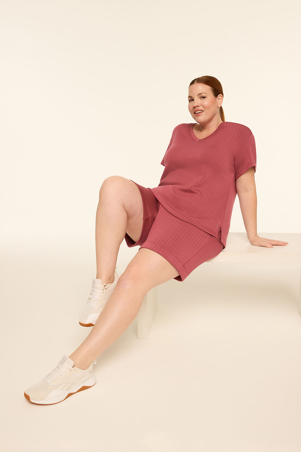 A woman in a mauve loungewear set and sneakers sits on a white cube against a plain, light background. Product Image 7