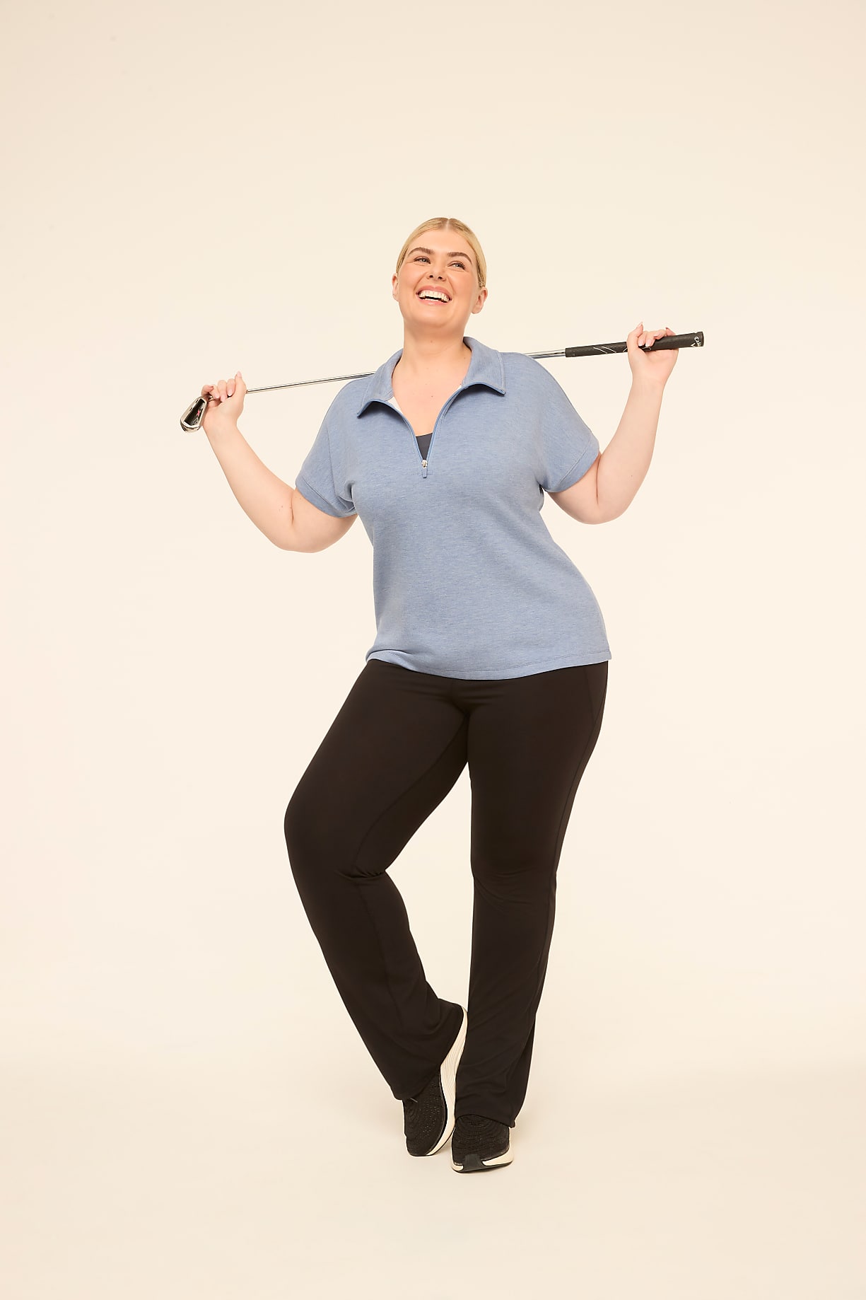 A smiling woman in athletic wear poses with a golf club against a plain, light-colored background. Product Image 9
