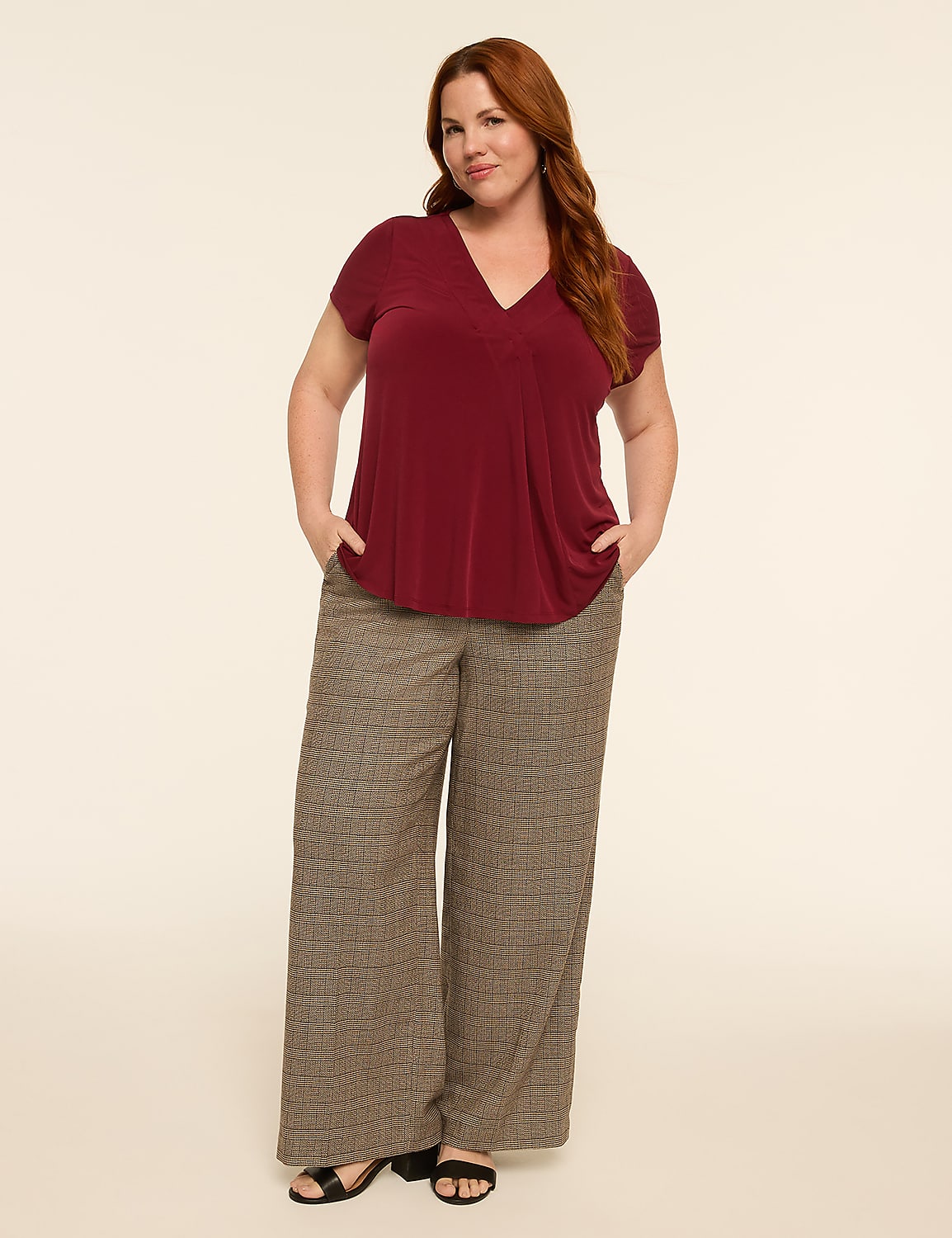 A woman with auburn hair stands with her hands in the pockets of her wide-leg patterned pants and a maroon V-neck top, against a plain, light-colored background. Product Image 3