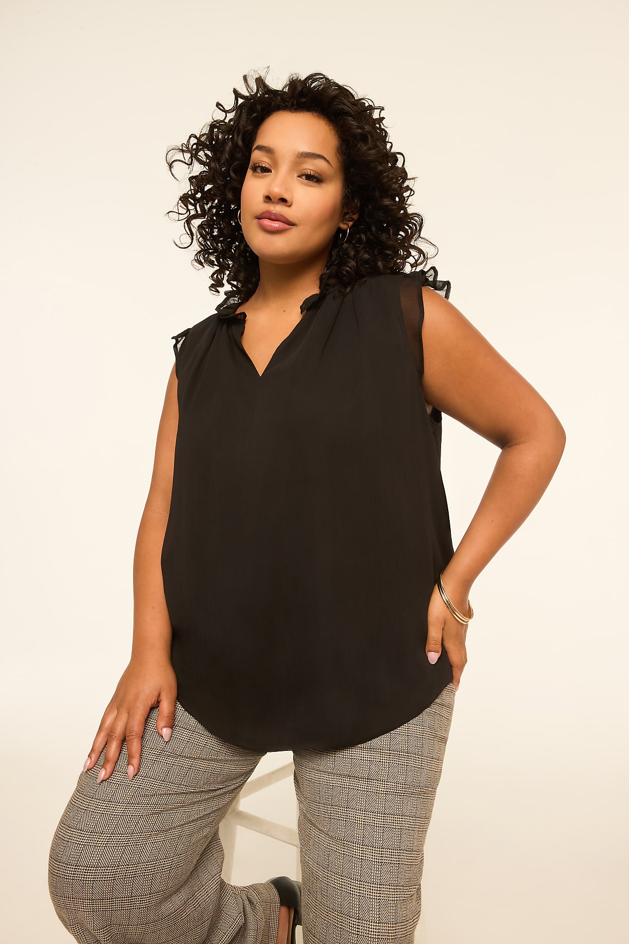 A woman with curly dark hair and a black top poses against a plain, light-colored background. Product Image 8