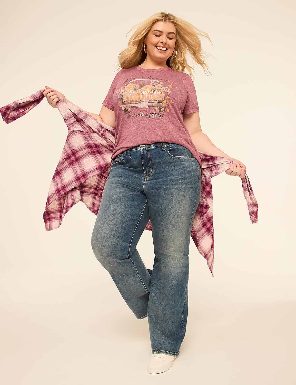 A smiling woman in a graphic tee and jeans poses with a plaid shirt draped over her arms against a plain, light-colored background. Product Image 3