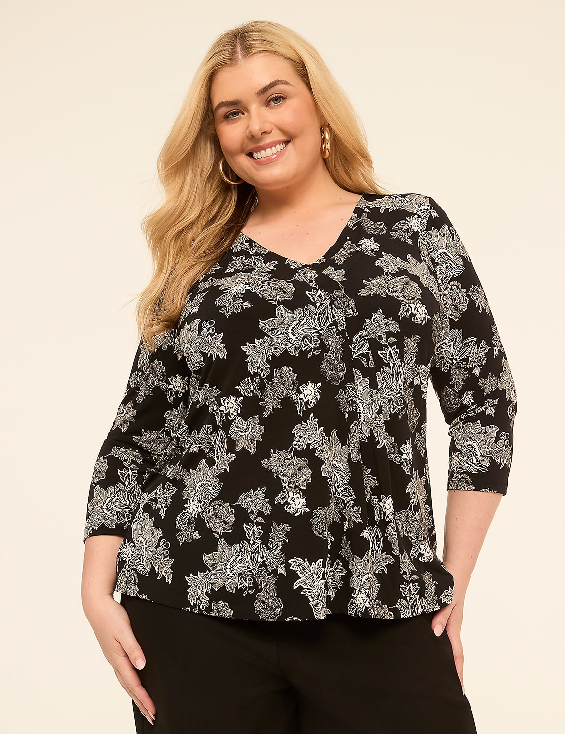 A smiling woman with blonde hair and a black and white floral top stands against a plain, light-colored background. Product Image 1