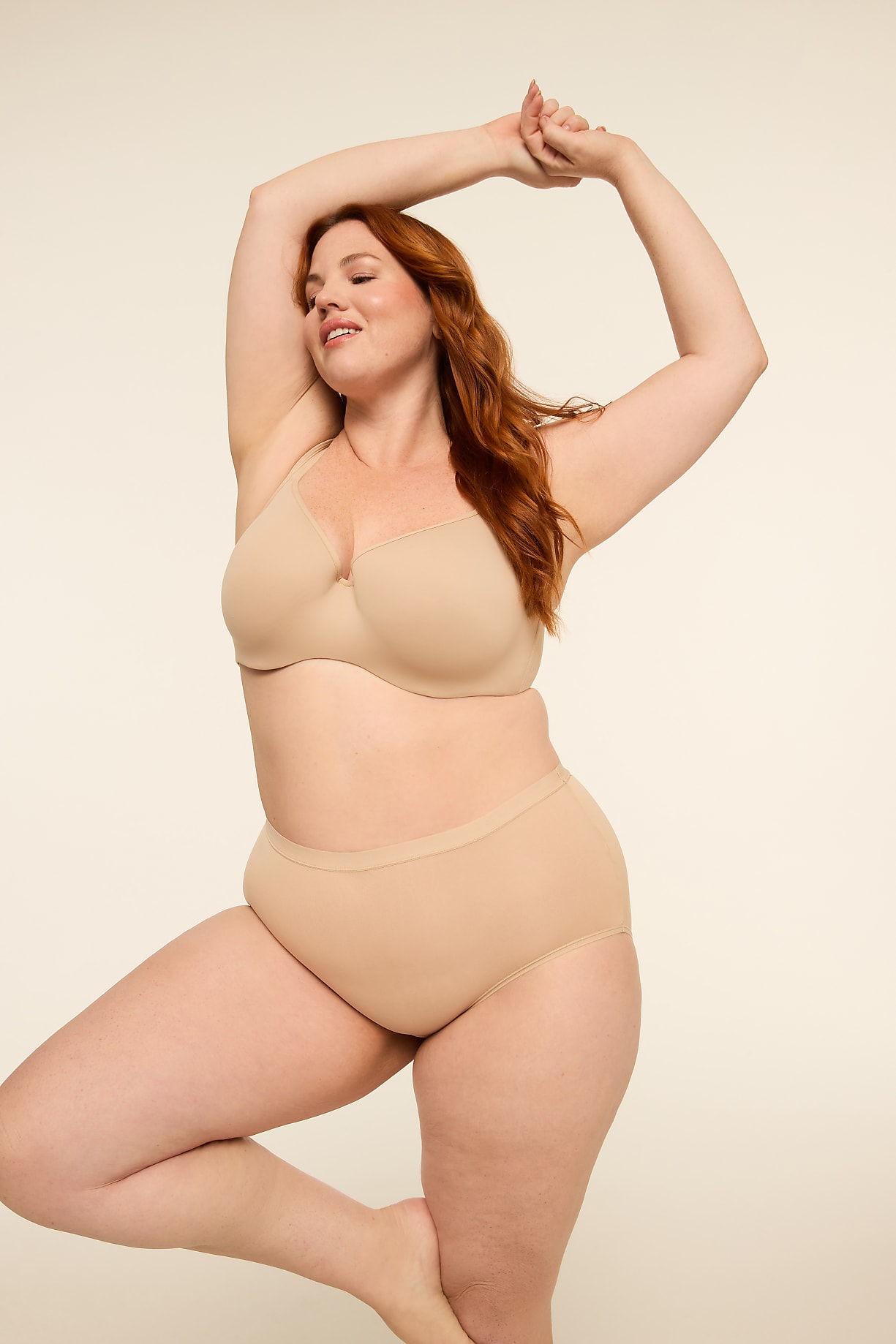 A woman with red hair in a beige bra and underwear poses with her arms raised against a plain, light background. Product Image 6