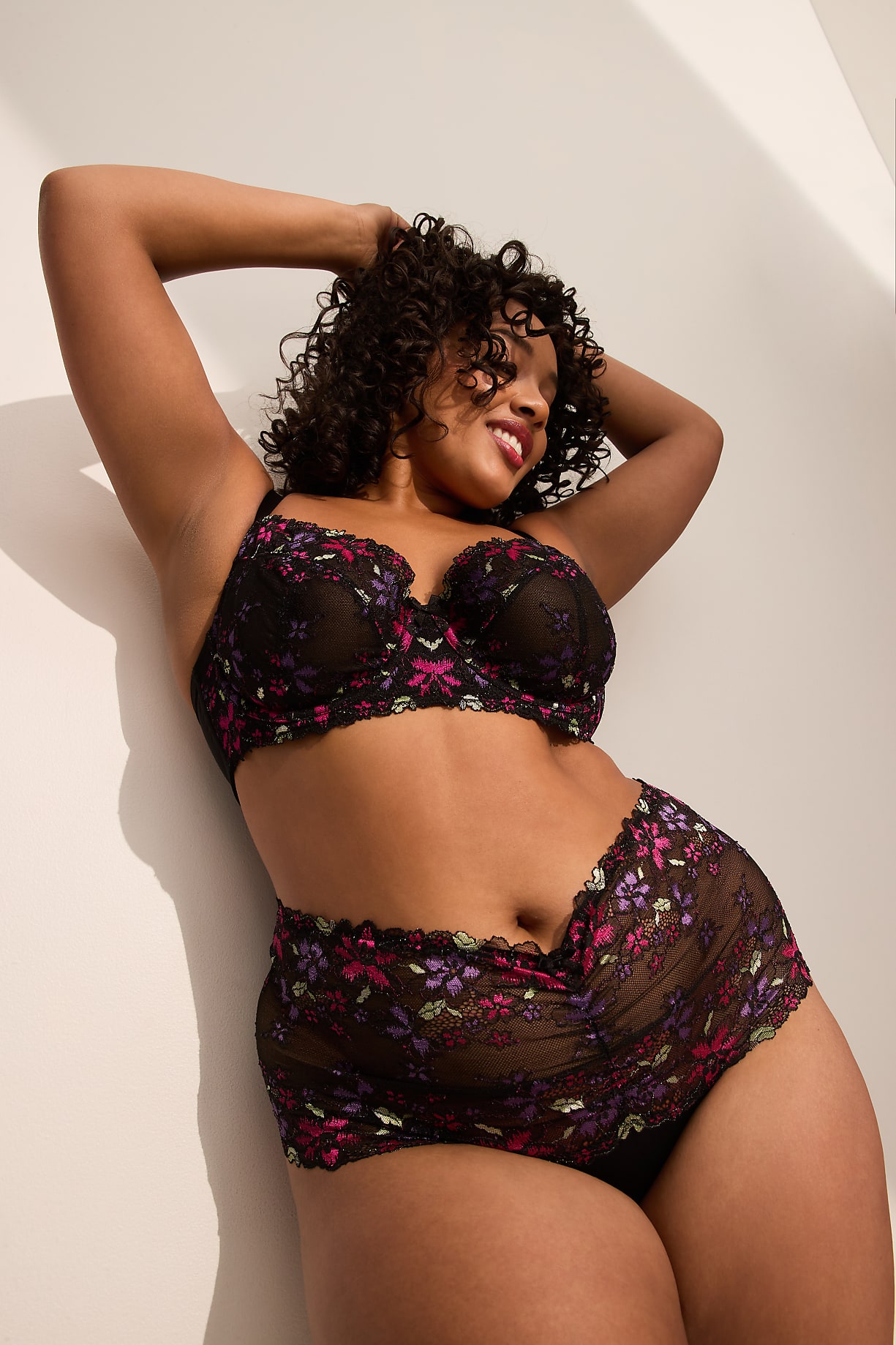 A woman in a floral lace bra and high-waisted briefs leans against a white wall. Product Image 6