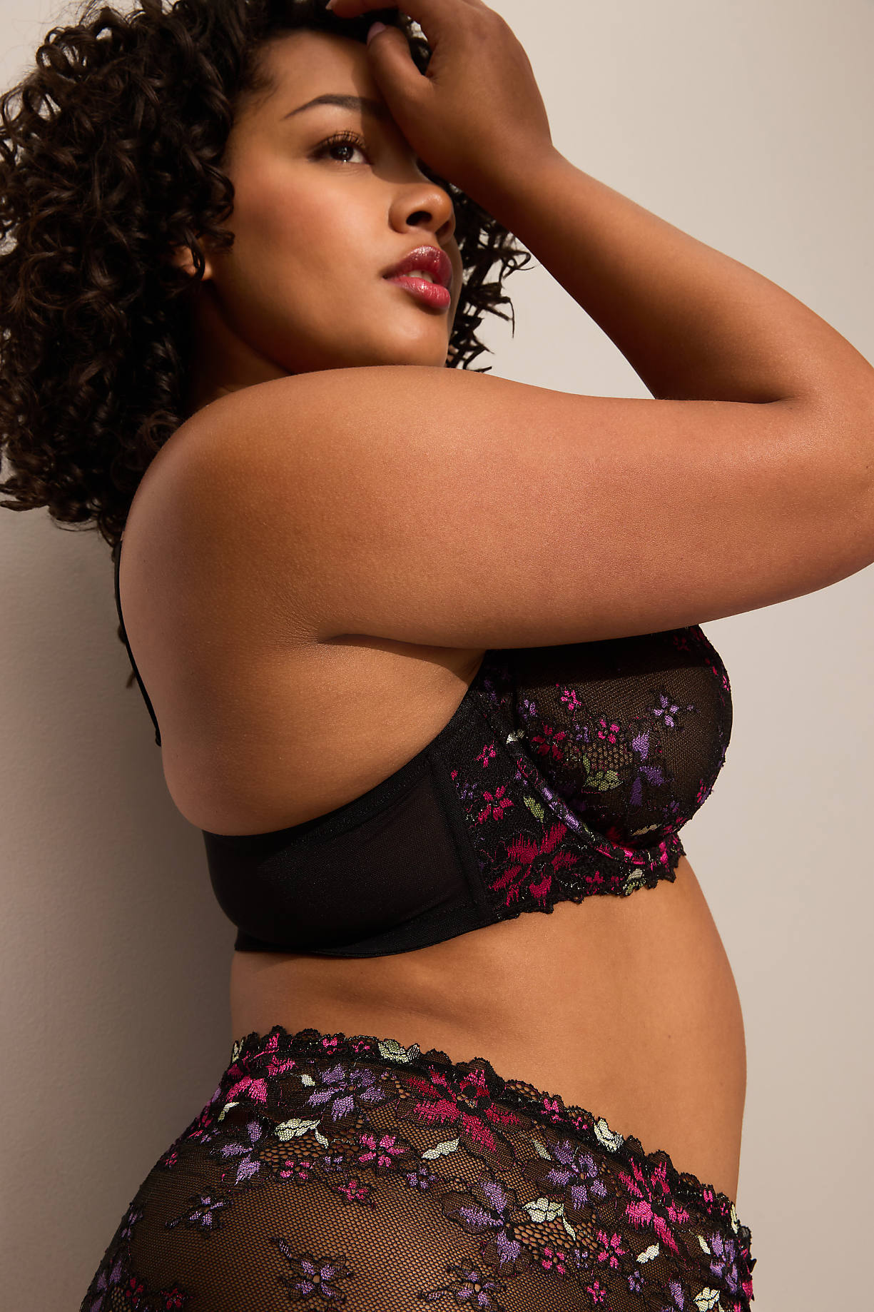 A woman with curly dark hair poses in a black floral bra and matching underwear against a plain, light-colored background. Product Image 7