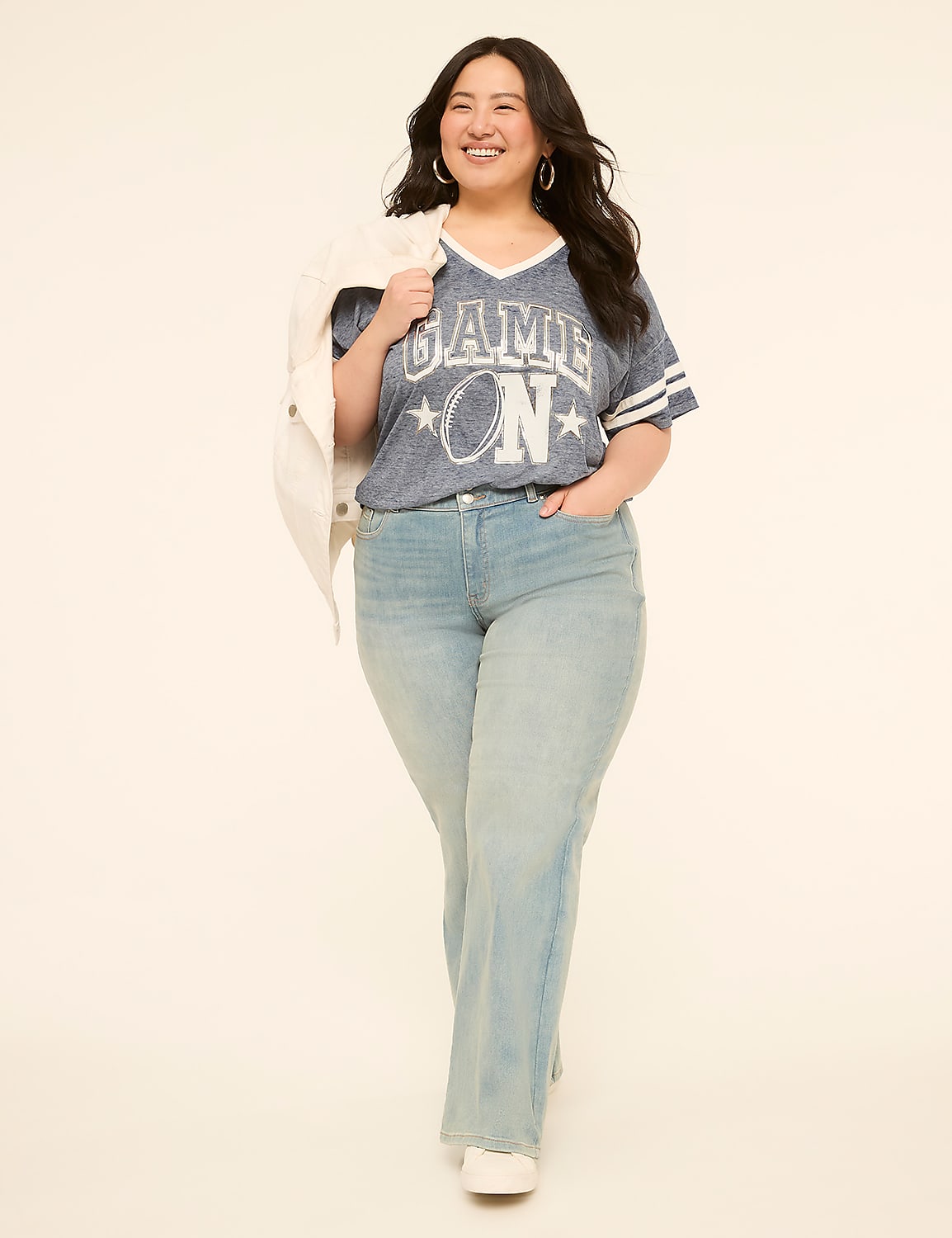 A smiling woman in a blue graphic t-shirt and light wash jeans walks forward against a plain, light-colored background. Product Image 3