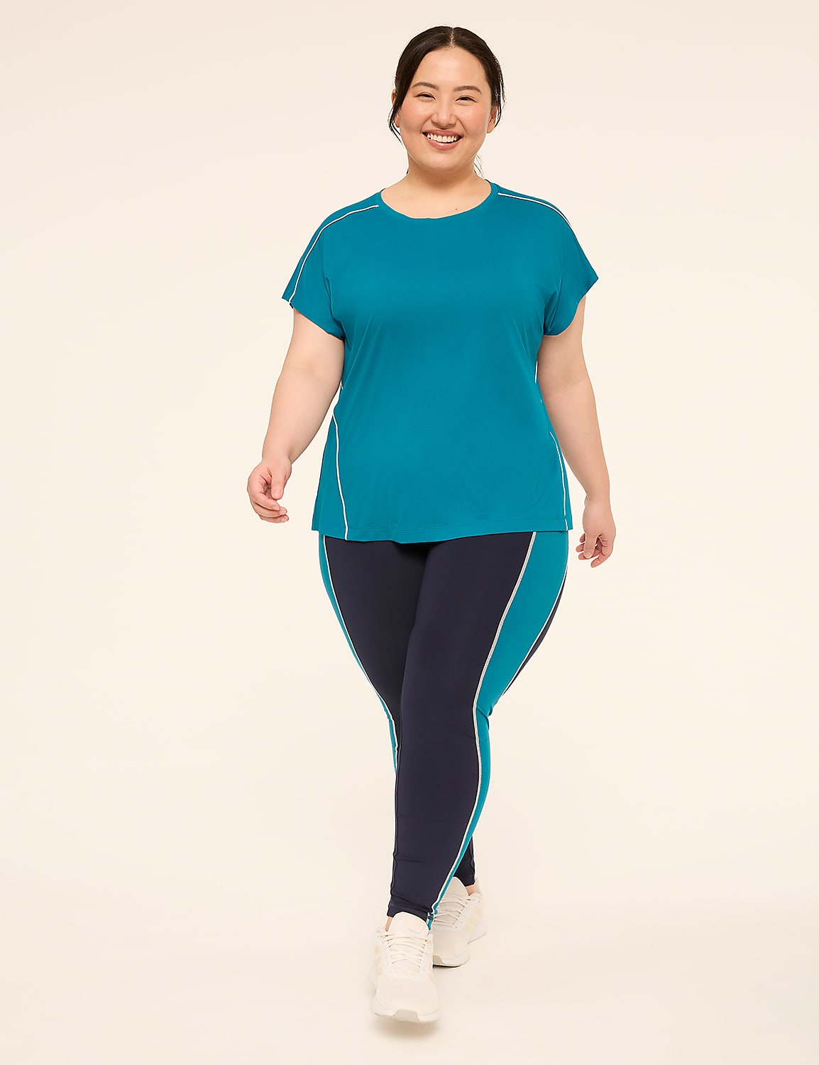 A smiling woman in teal athletic wear walks forward against a plain, light background. Product Image 3