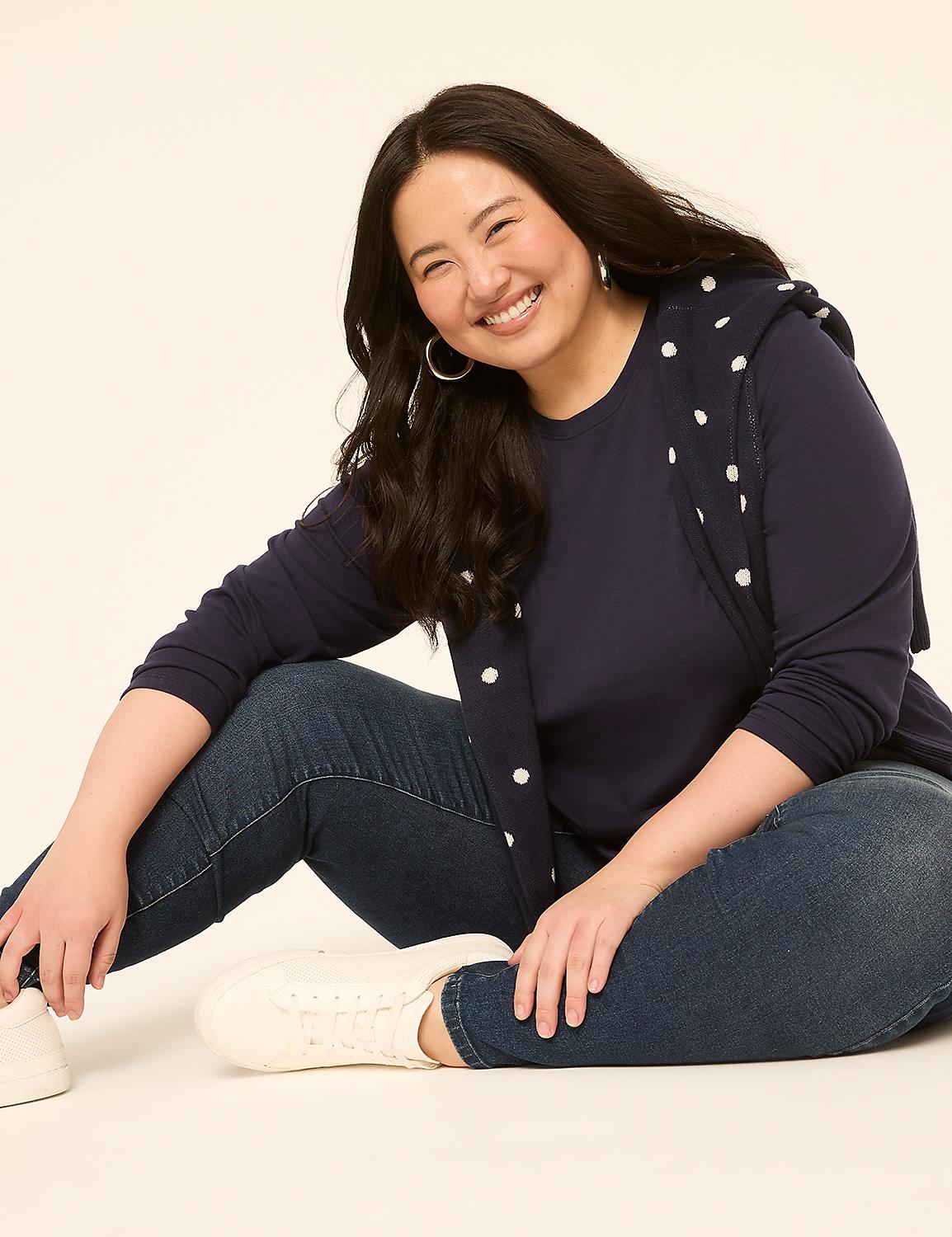 A smiling woman in a navy polka-dot sweater and jeans sits on a plain, light-colored background. Product Image 3