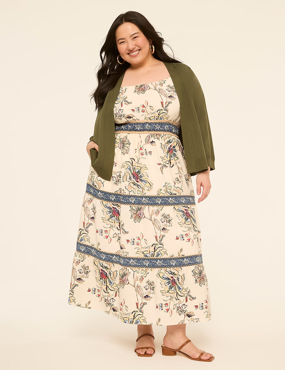 A smiling woman in a floral dress and olive green cardigan stands against a plain, light-colored background. Product Image 4