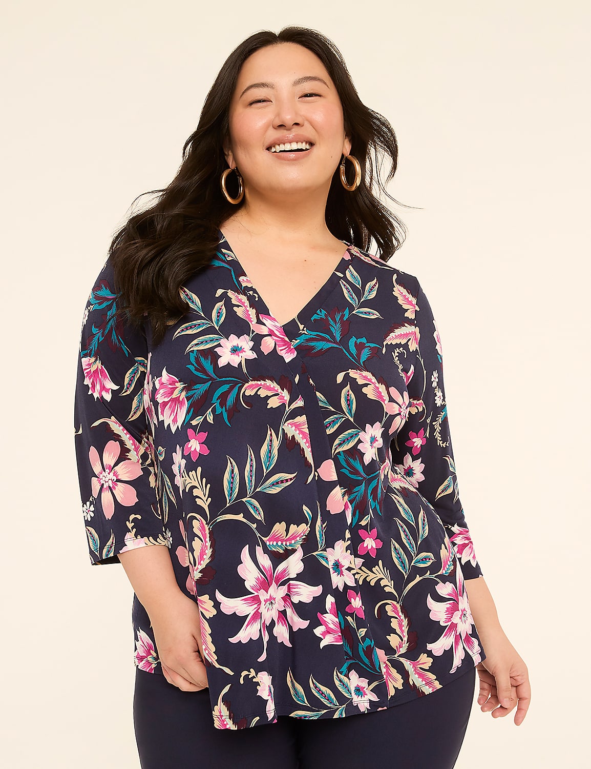 A smiling woman in a floral navy blue top stands against a plain cream background. Product Image 1
