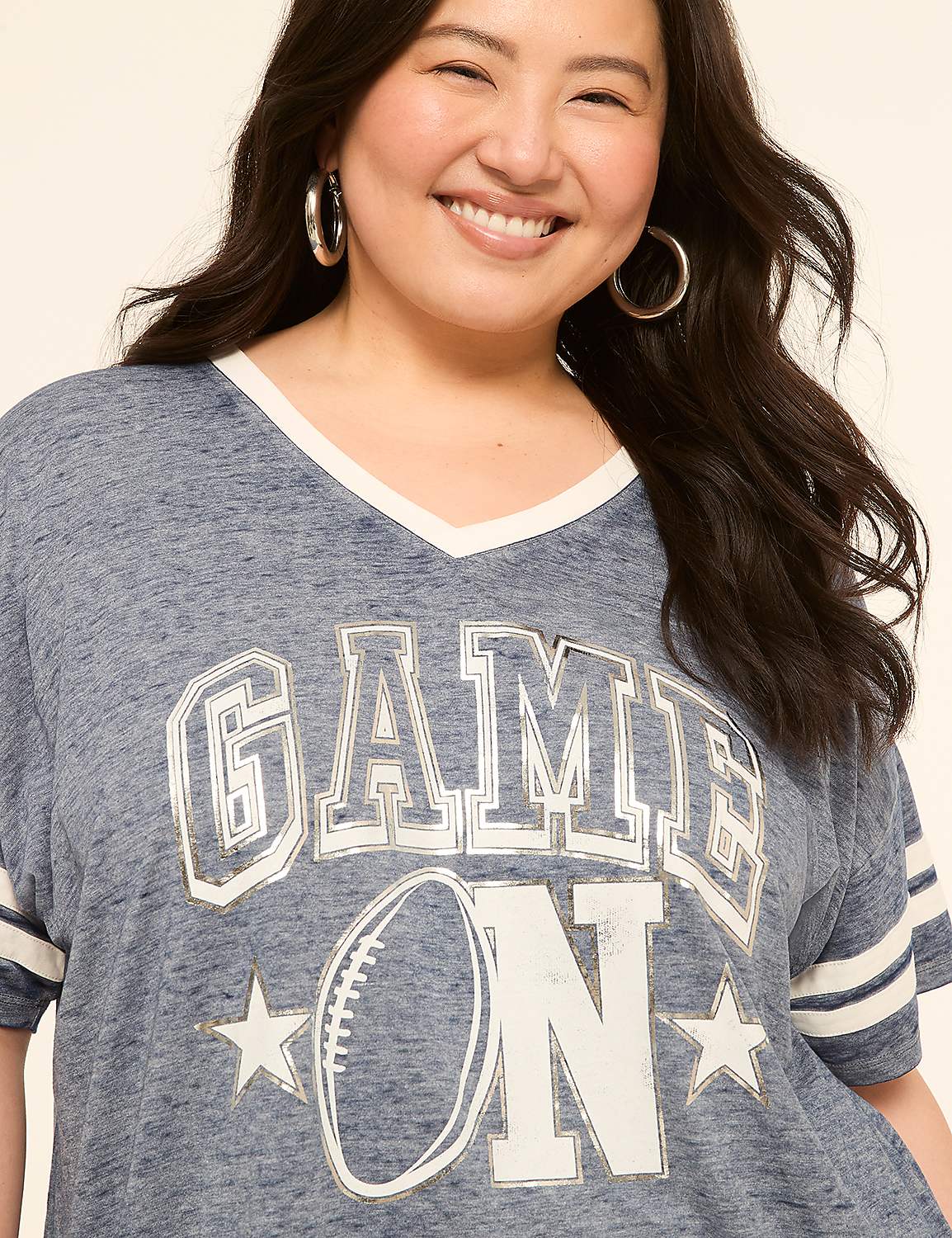 A smiling woman in a blue "GAME ON" t-shirt with a football graphic stands against a plain, light-colored background. Product Image 4