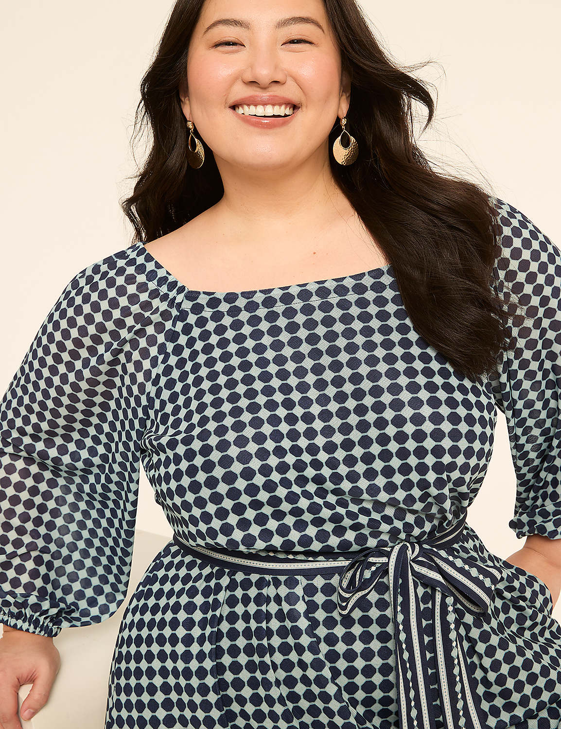 A smiling woman with dark hair wears a blue and white polka dot dress with a square neckline and a matching belt, against a plain, light background. Product Image 3