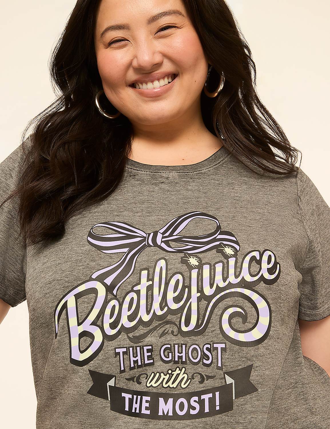 A smiling woman in a grey t-shirt with "Beetlejuice the ghost with the most!" printed on it poses against a plain, light-colored background. Product Image 4