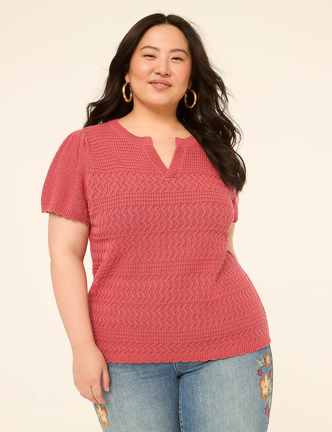 A woman in a pink textured top and embroidered jeans smiles against a plain cream background. Product Image 1