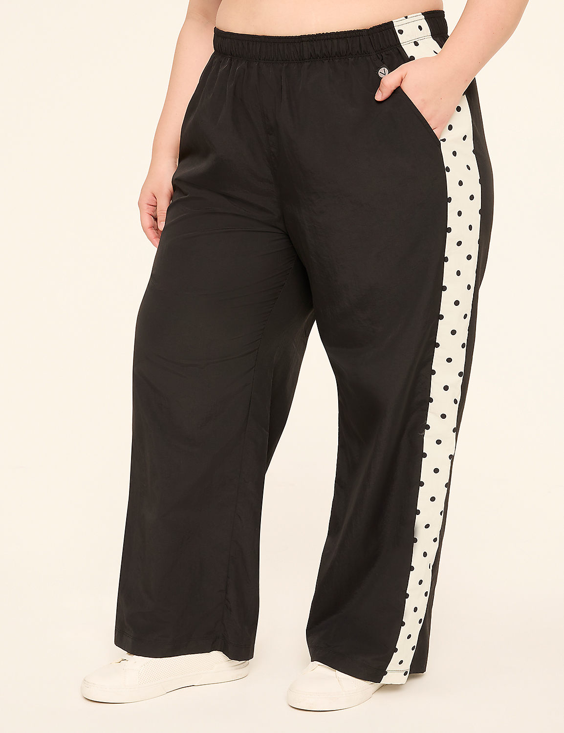 A person wearing black wide-leg pants with a white side stripe featuring black polka dots stands against a plain, light-colored background. Product Image 1