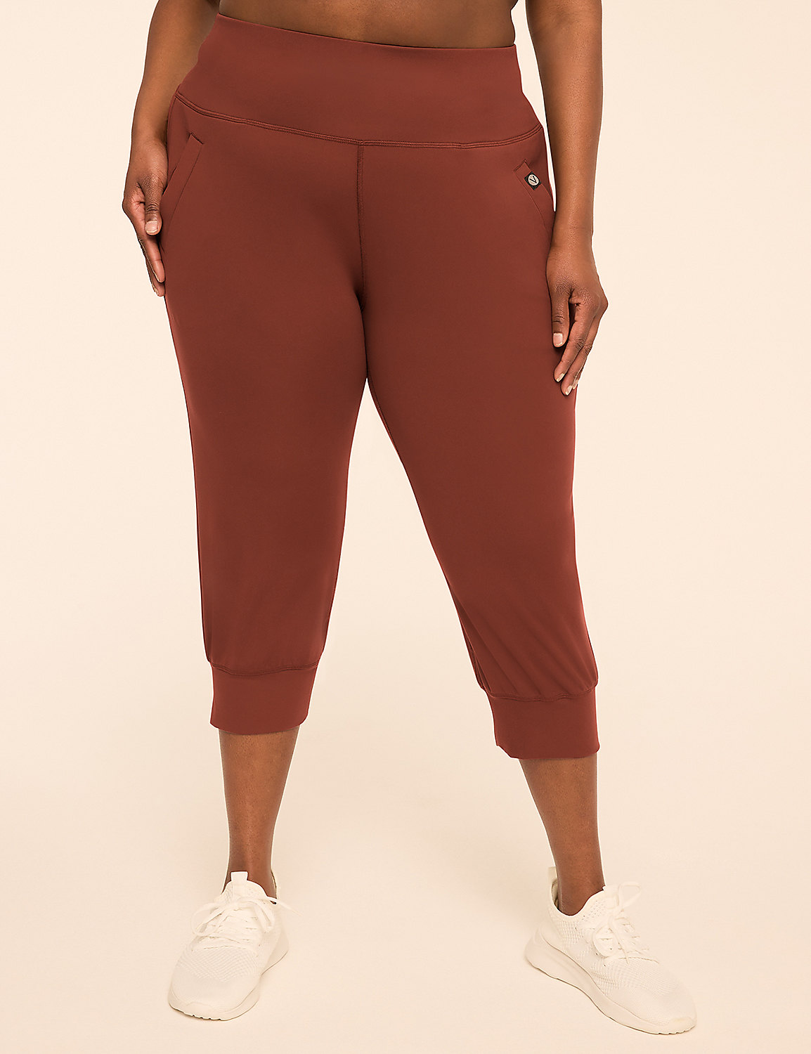 A person wearing rust-colored capri pants and white sneakers stands against a plain, light brown background. Product Image 1