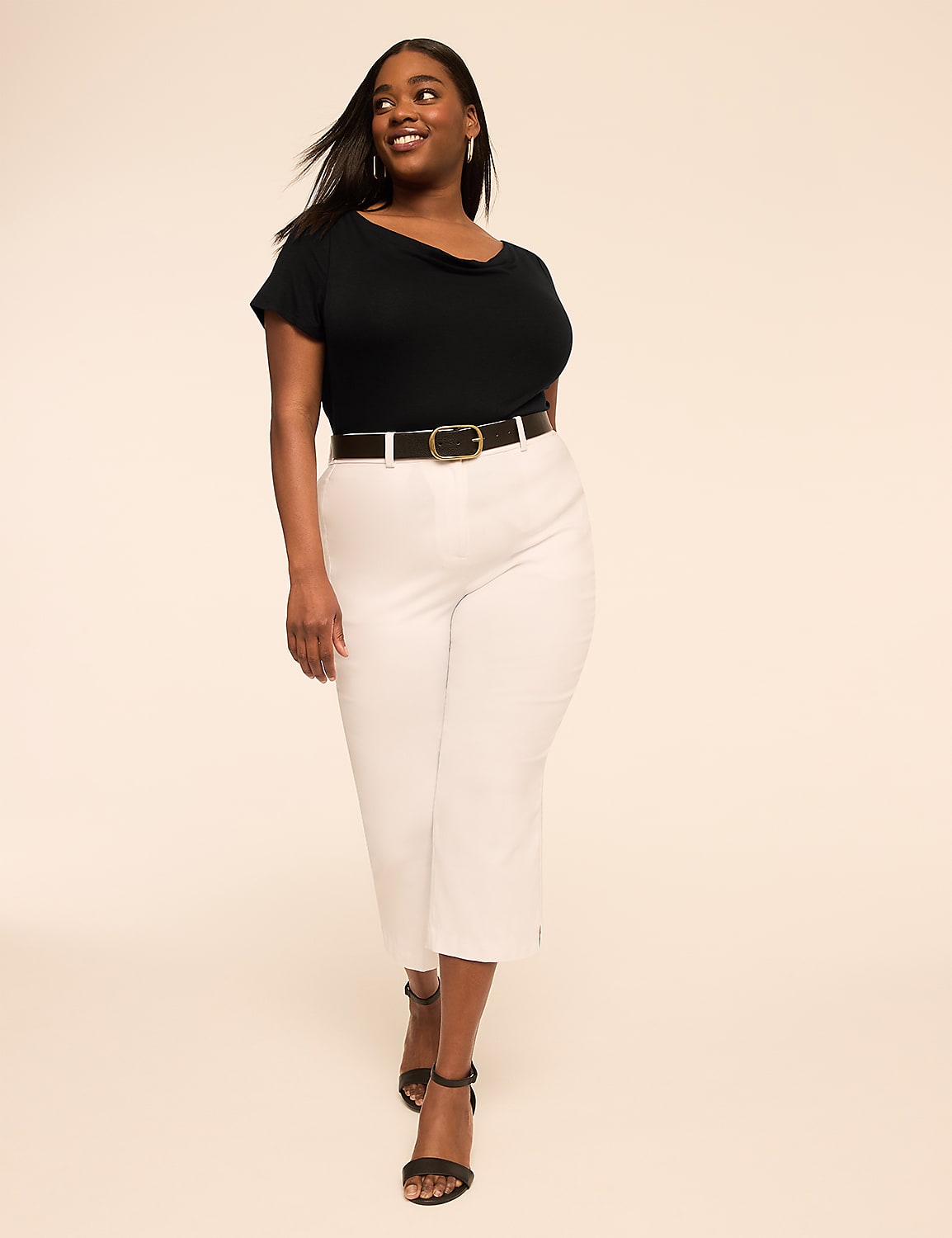 A smiling woman in a black top and white capri pants walks forward against a plain, light-colored background. Product Image 3