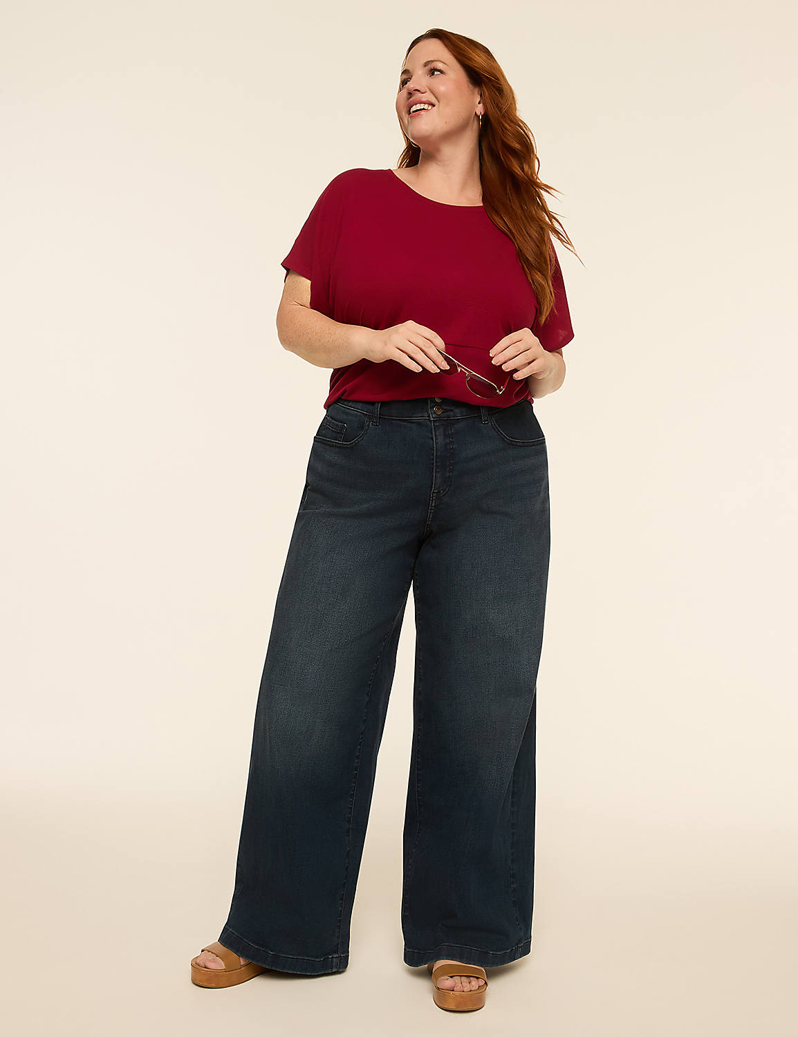 A smiling woman with auburn hair stands in the foreground wearing a maroon t-shirt and wide-leg jeans against a plain, light-colored background. Product Image 3