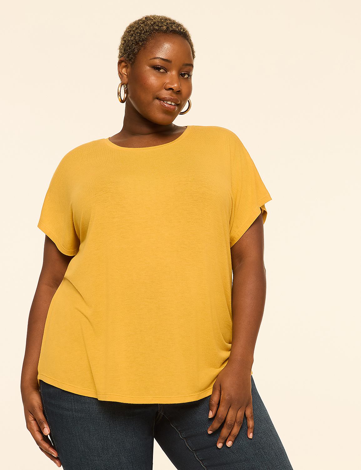 A woman with short, blonde hair and hoop earrings smiles at the camera, wearing a mustard yellow t-shirt and blue jeans against a plain, light beige background. Product Image 1