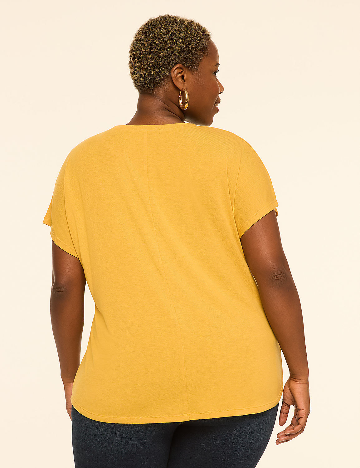 A woman in a mustard yellow t-shirt and dark jeans stands against a plain cream background. Product Image 2