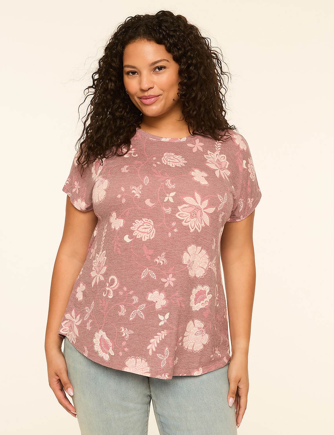 A woman with curly dark hair smiles at the camera, wearing a pink floral t-shirt and light blue jeans against a plain, light-colored background. Product Image 1