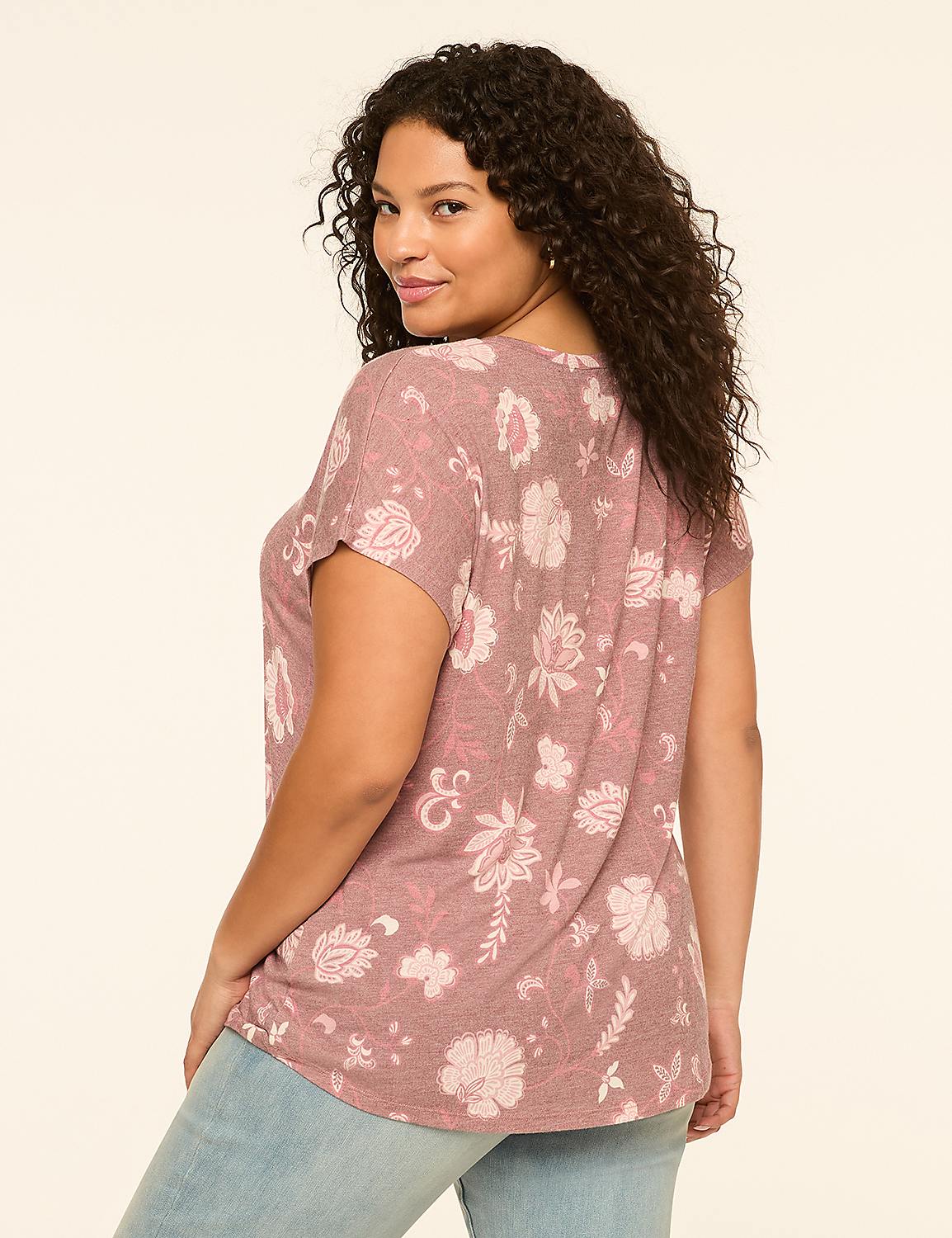 A woman with curly dark hair, wearing a floral print top and light blue jeans, poses against a plain, light-colored background. Product Image 2