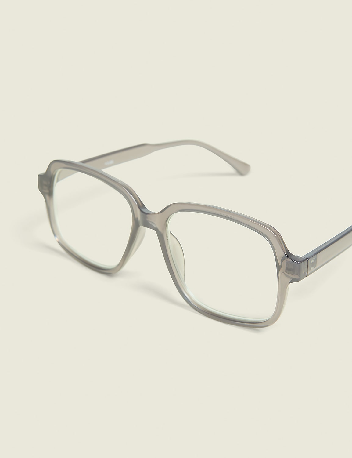 A pair of translucent gray square-framed glasses rests on a pale, neutral background. Product Image 1