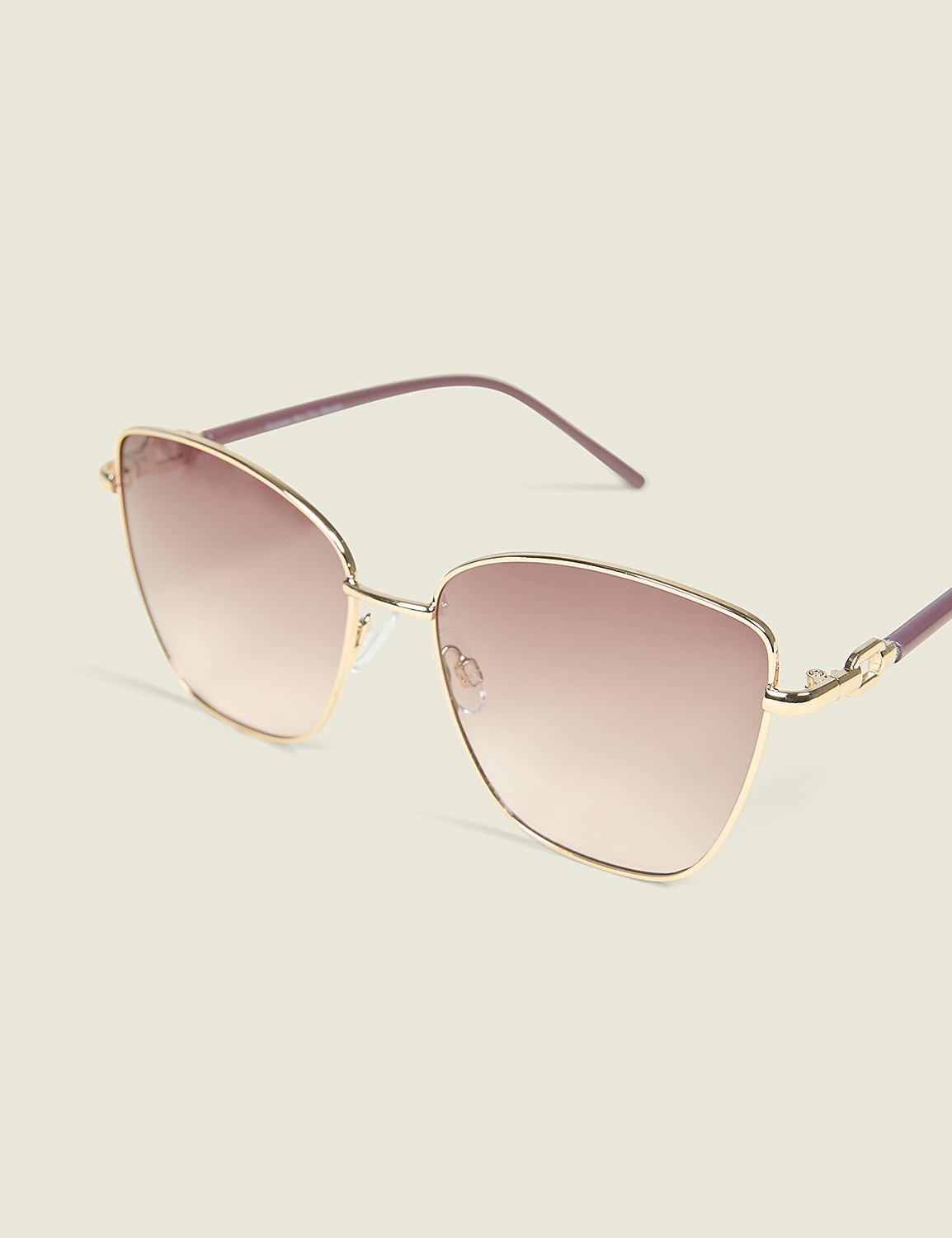 A pair of rose-gold cat-eye sunglasses with gradient lenses rests on a pale yellow background. Product Image 1