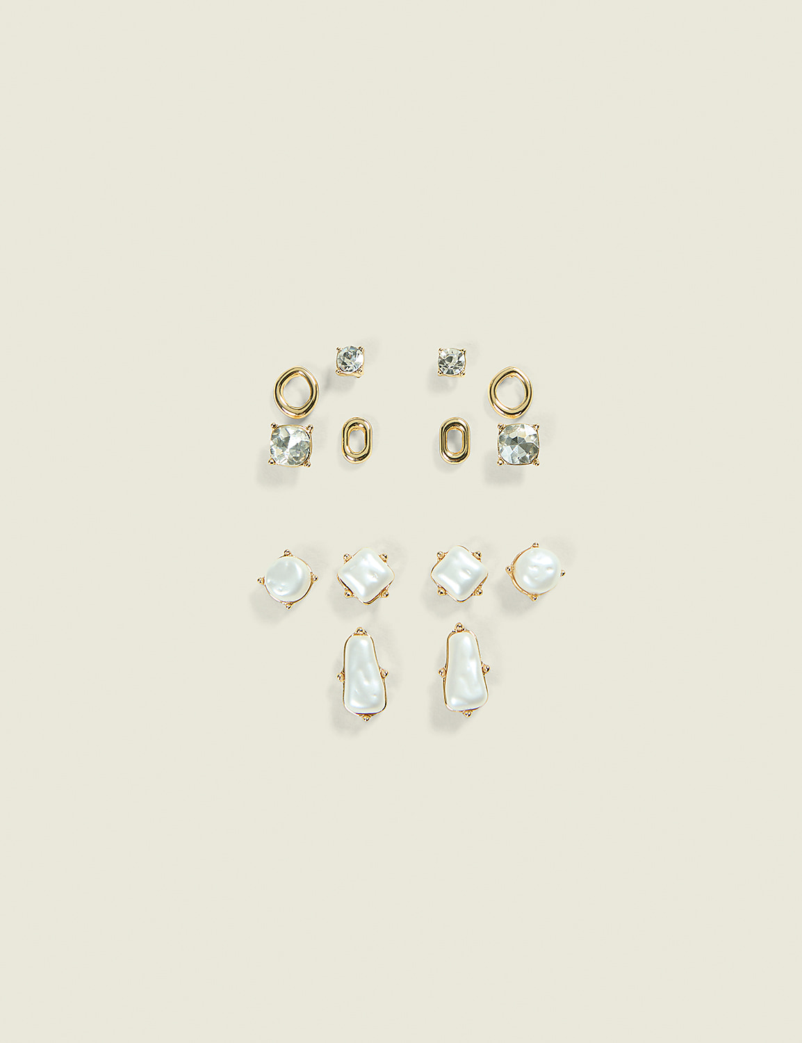 A collection of assorted gold earrings with clear stones and pearls are arranged on a pale cream background. Product Image 1