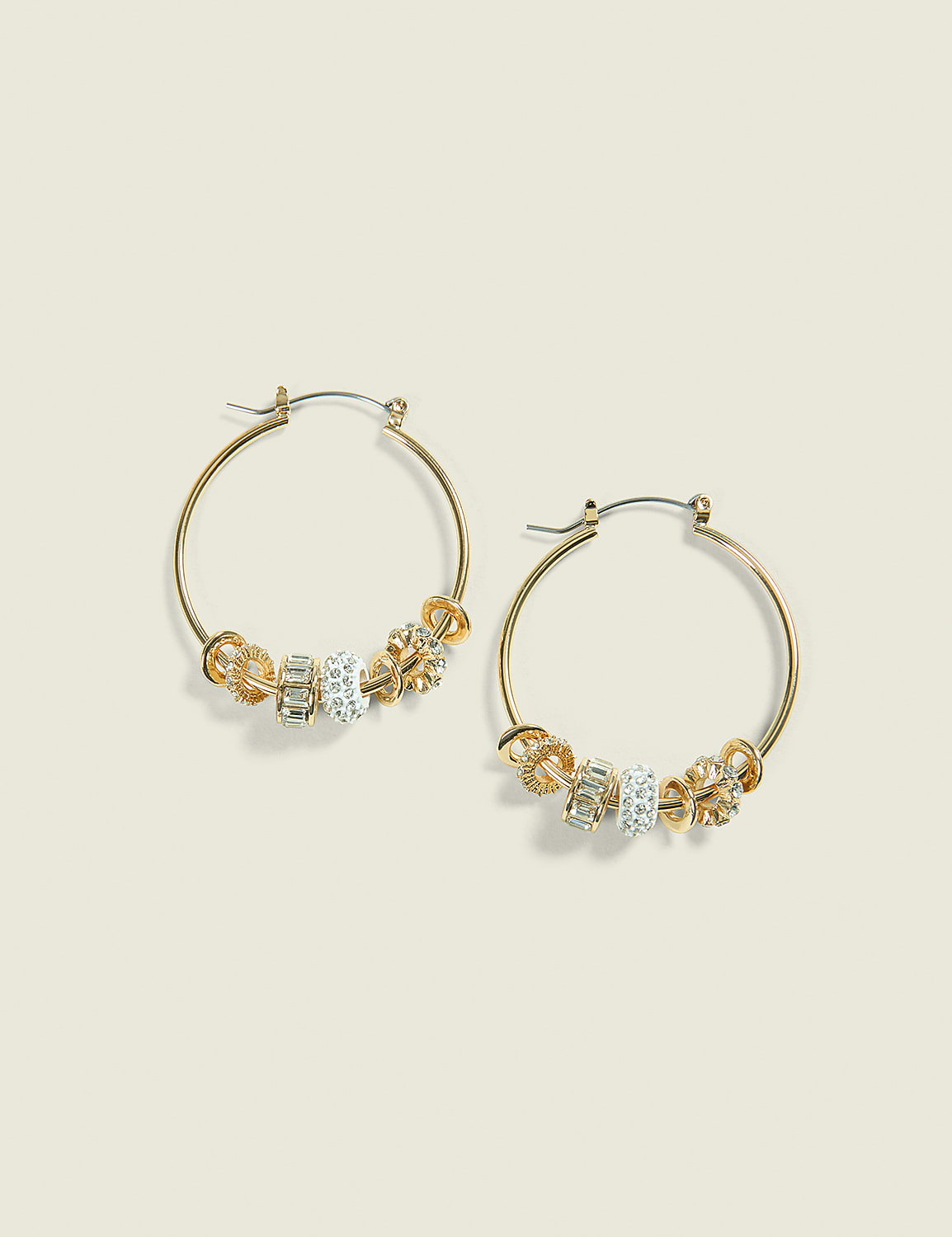 Gold hoop earrings with clear and gold beads, and floral charms, are displayed against a pale yellow background. Product Image 1
