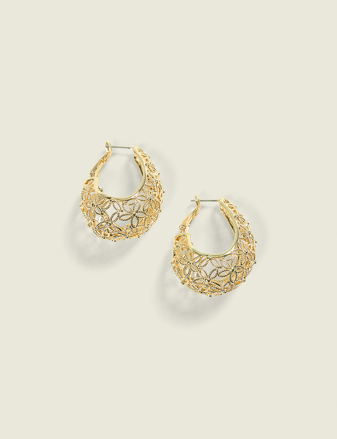 A pair of ornate gold hoop earrings with floral cutouts rests on a pale, neutral background. Product Image 1