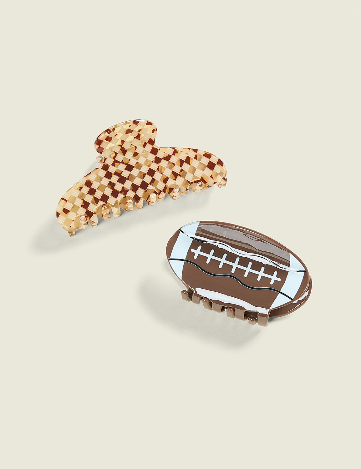 Two hair clips, one a checkered pattern and the other shaped like a football, rest on a light beige background. Product Image 1