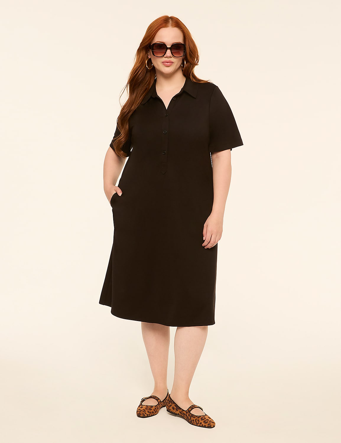 A woman with red hair and sunglasses stands in a black dress and leopard print flats against a plain, light-colored background. Product Image 1
