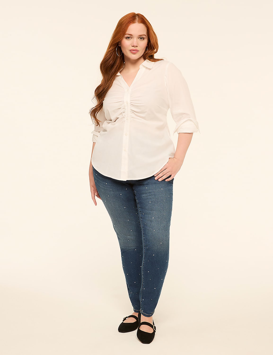 A woman with long red hair stands in the foreground wearing a white ruched blouse and jeweled jeans against a plain cream background. Product Image 3