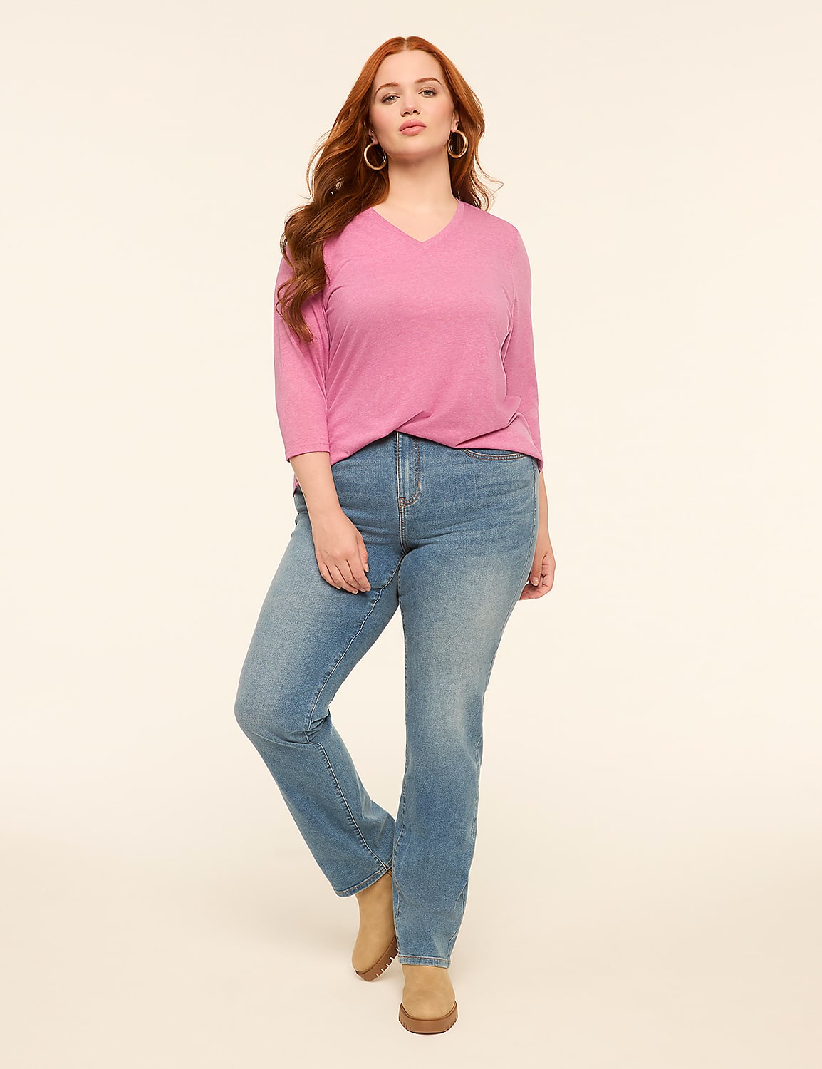 A woman with long red hair stands in the foreground wearing a pink v-neck shirt and blue jeans against a plain, light background. Product Image 3