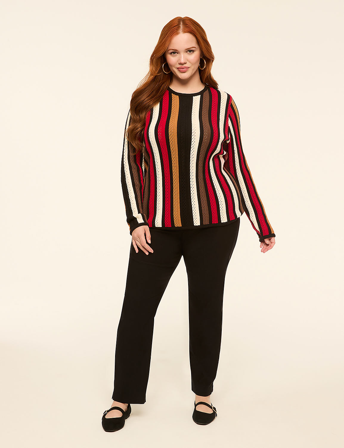 A woman with long red hair stands in the foreground wearing a striped sweater and black pants, against a plain, light-colored background. Product Image 3