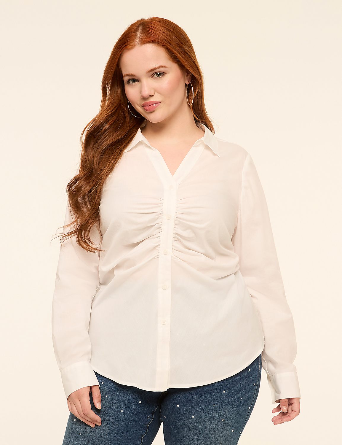 A woman with long, wavy red hair stands in the foreground wearing a white ruched blouse and jeweled jeans, against a plain, light-colored background. Product Image 1