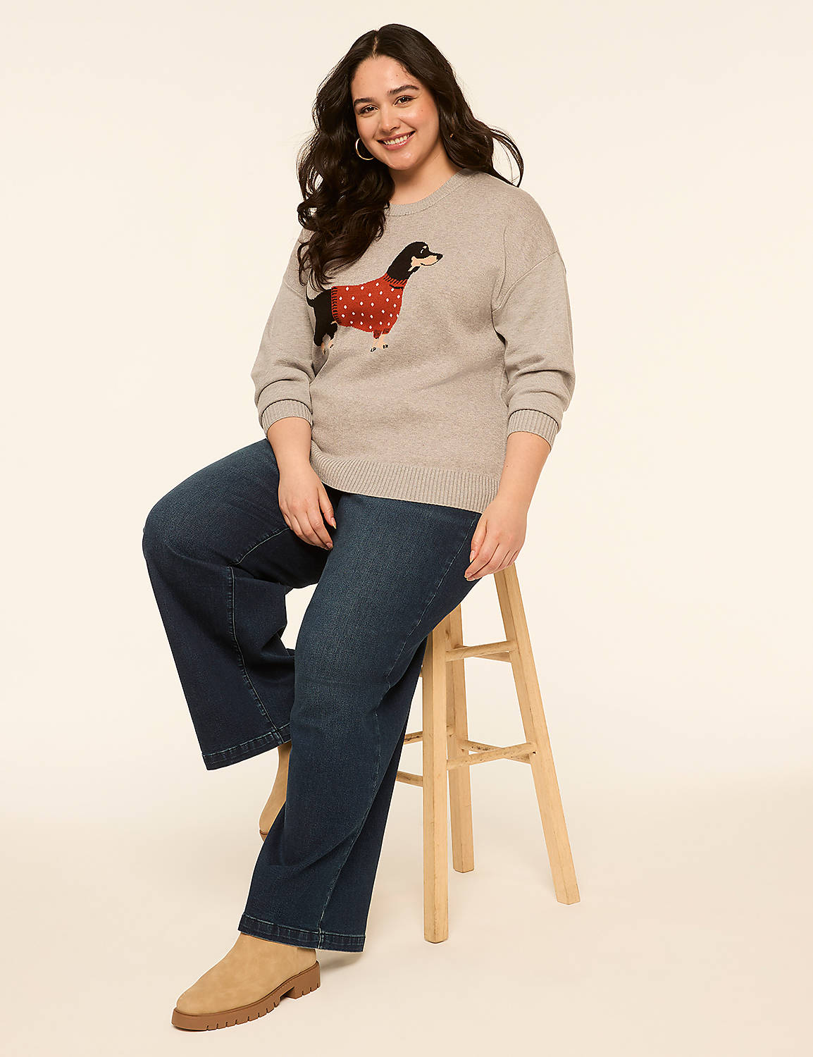 A woman in a dog-patterned sweater and wide-leg jeans sits on a stool against a plain, light-colored background. Product Image 3