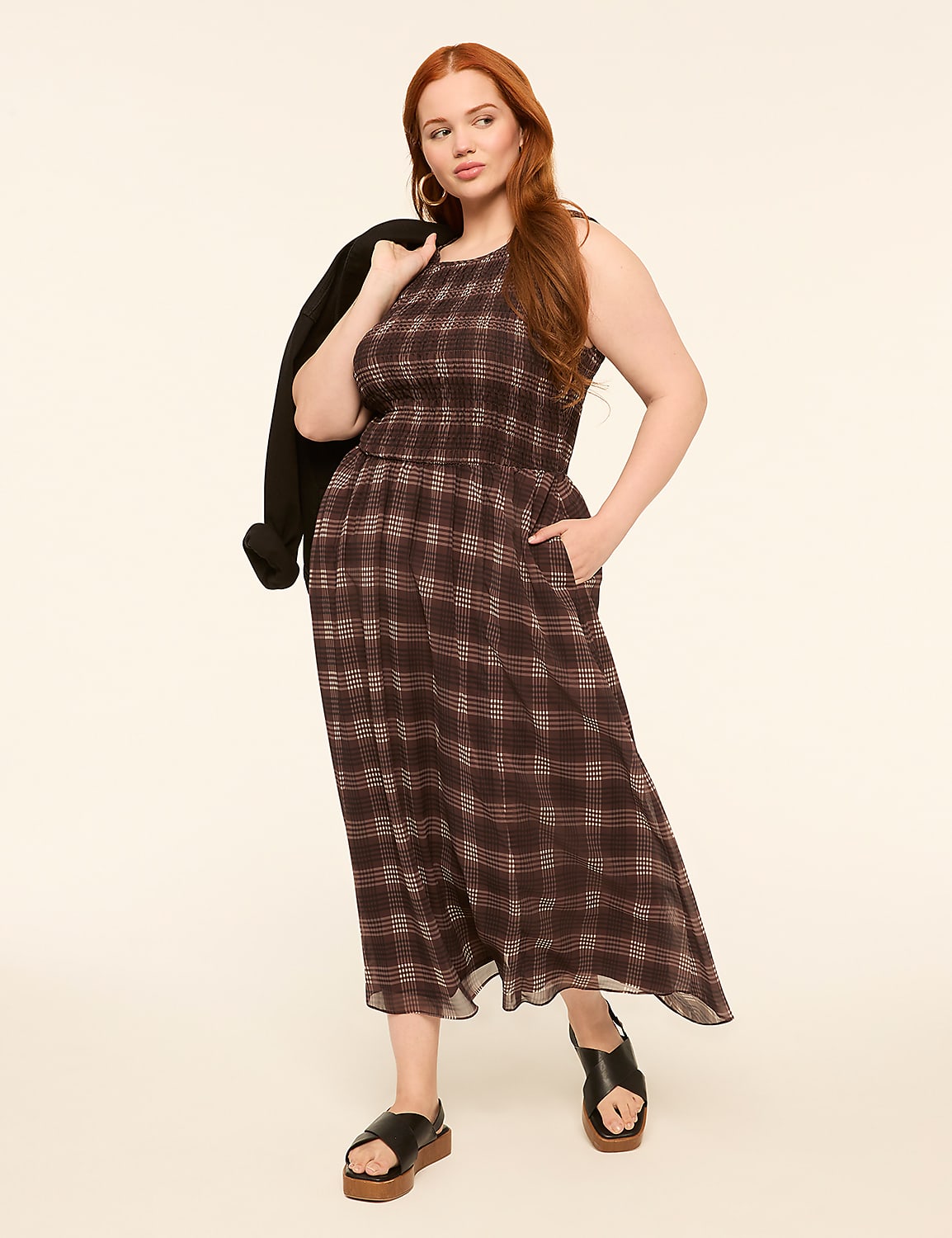 A woman in a plaid dress and sandals stands against a plain, light-colored background with a jacket draped over her shoulder. Product Image 1