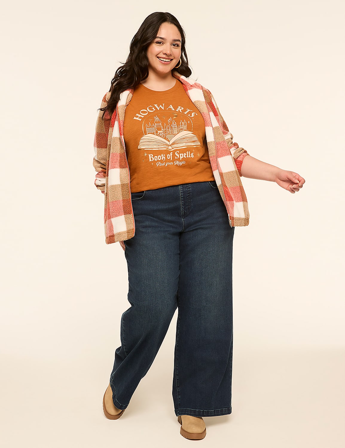 A smiling woman in a Hogwarts t-shirt and wide-leg jeans stands against a plain, light-colored background. Product Image 3