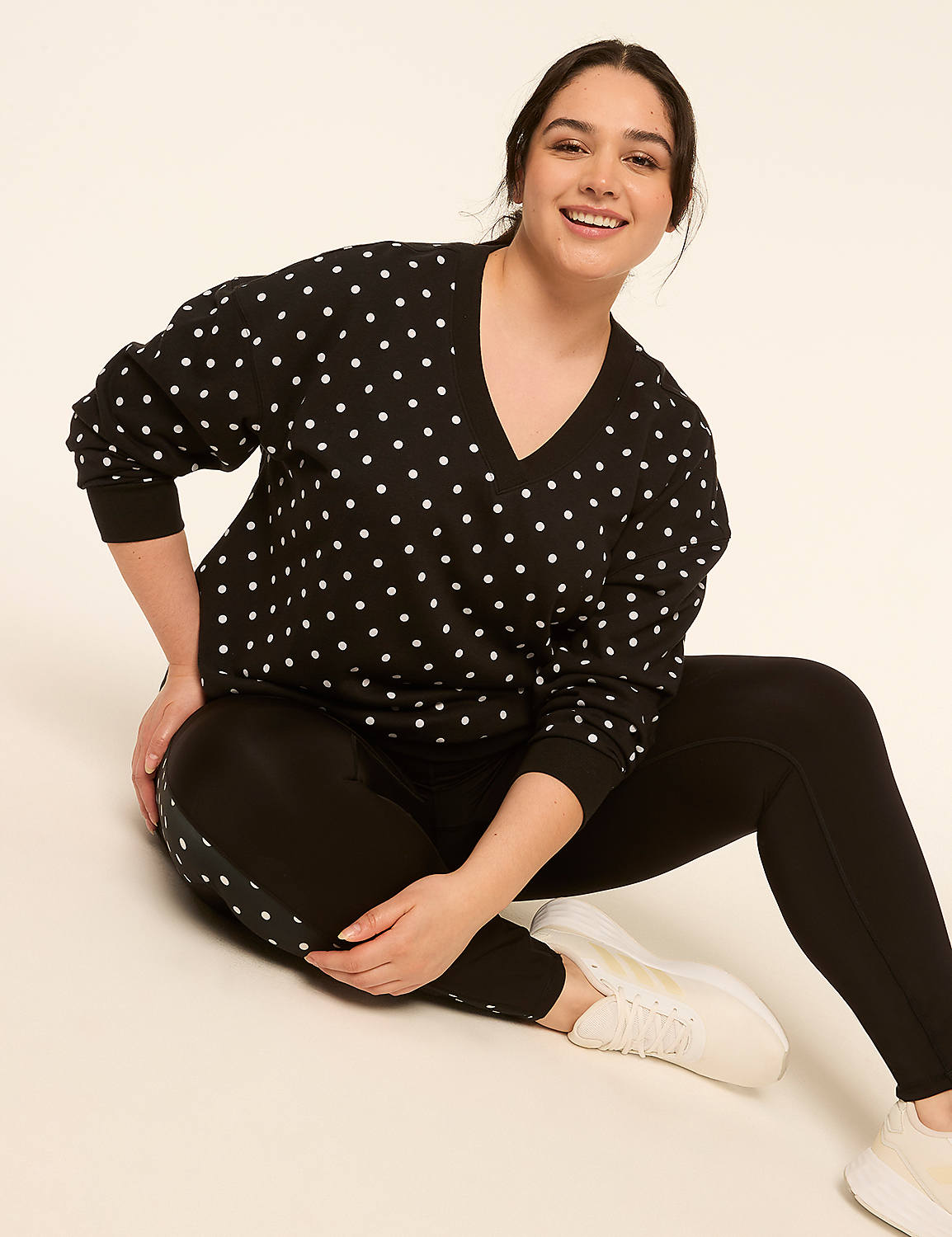 A smiling woman in a polka dot sweater and black leggings sits on a plain, light-colored background. Product Image 3