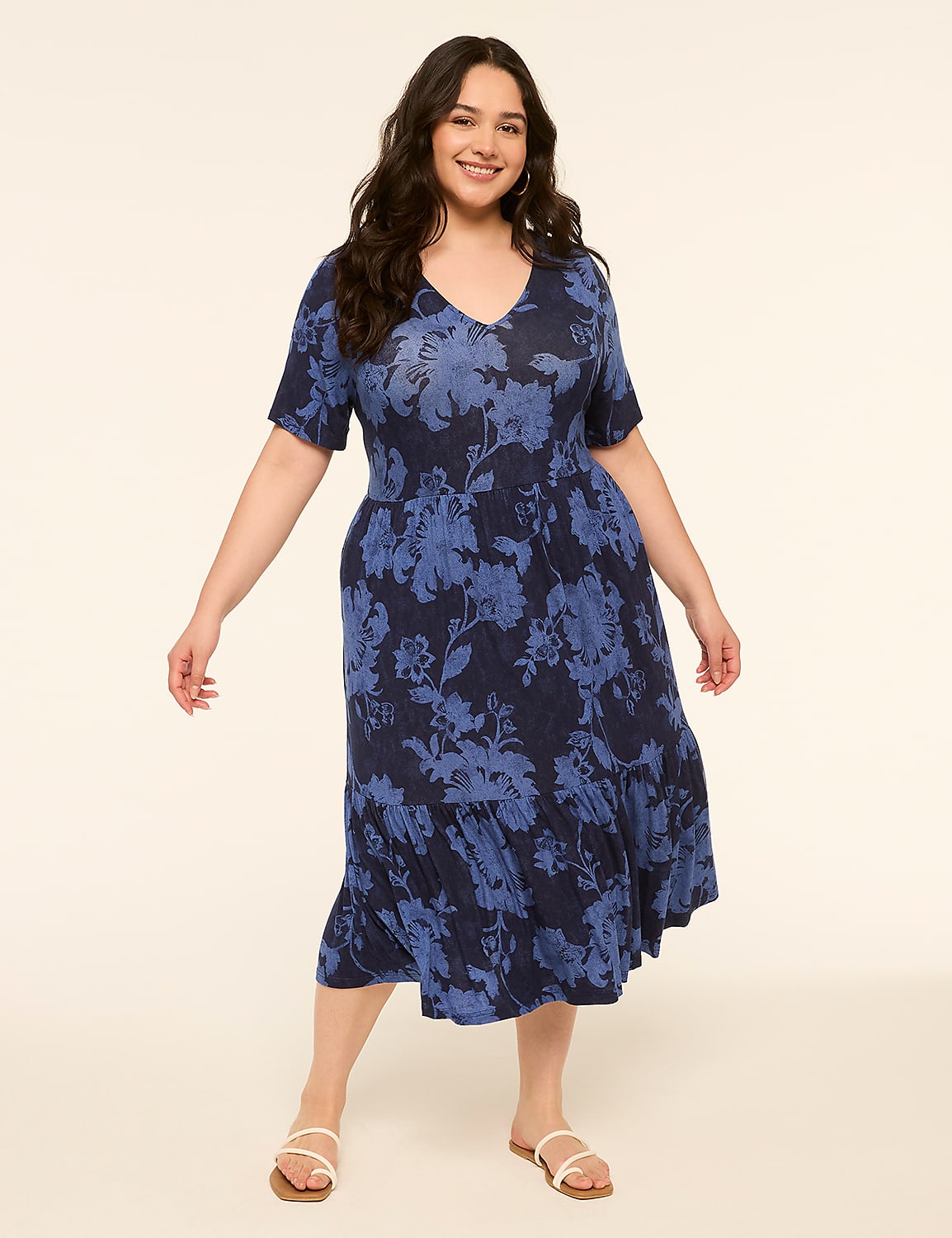 A smiling woman in a blue floral dress stands against a plain, light-colored background. Product Image 1