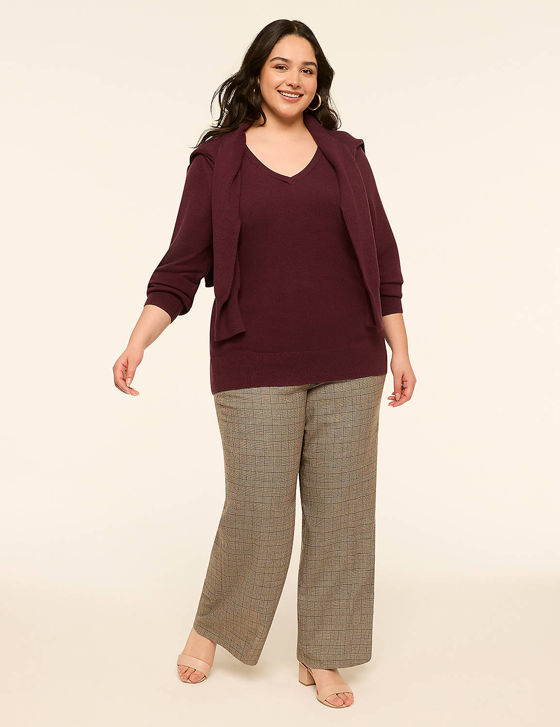 A smiling woman in a burgundy v-neck sweater and plaid pants stands against a plain, light-colored background. Product Image 3