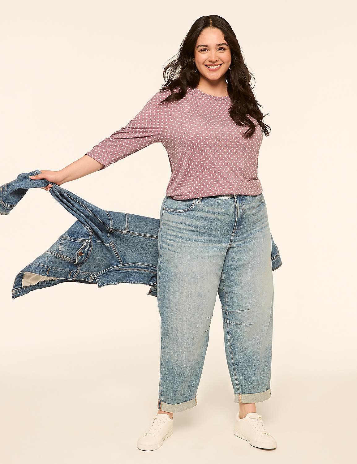 A smiling woman in a polka-dot shirt and baggy jeans stands against a plain, light-colored background, holding a denim jacket. Product Image 3