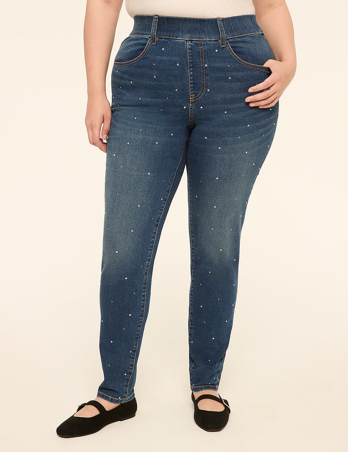 A person wearing studded denim jeans and black ballet flats stands against a plain, light-colored background. Product Image 1