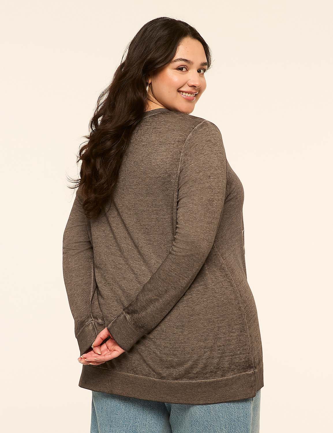 A woman with dark hair and a brown sweater stands with her hands behind her back against a plain, light-colored background. Product Image 2