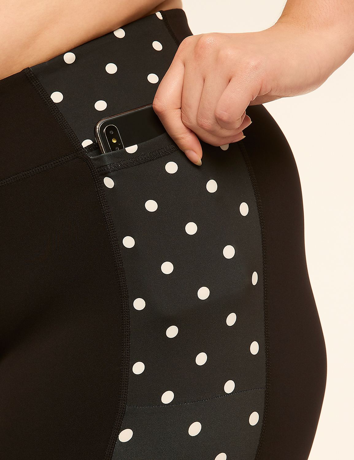 A hand tucks a smartphone into the polka-dotted pocket of black leggings against a plain background. Product Image 4