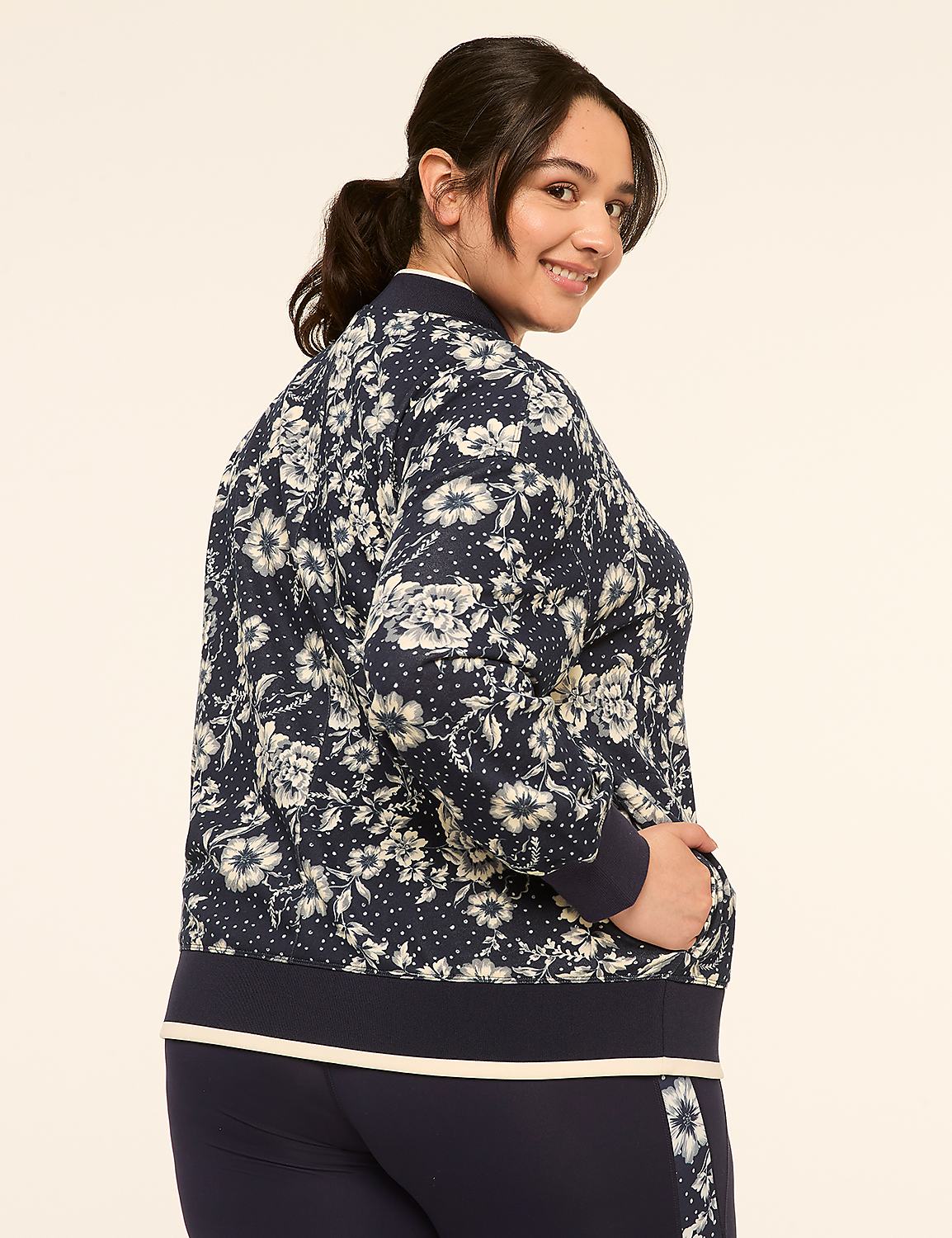 A woman in a floral bomber jacket and navy pants smiles over her shoulder against a plain, light background. Product Image 2