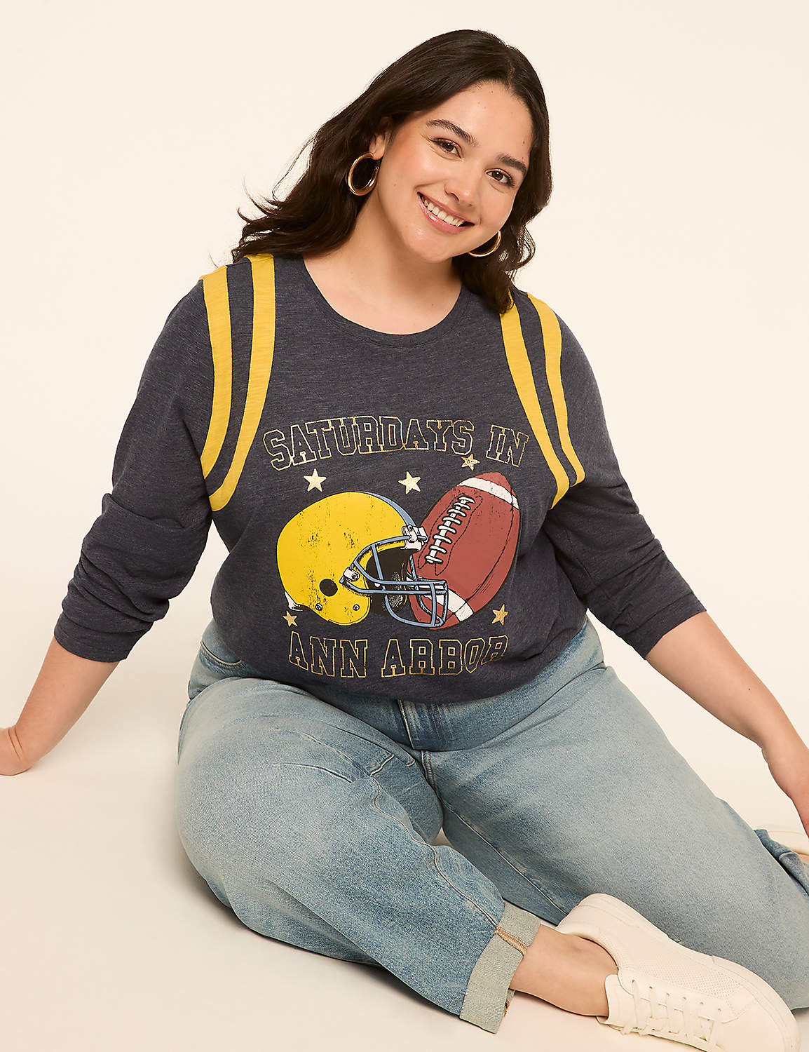 A smiling woman in a graphic t-shirt and jeans sits against a plain, light-colored background. Product Image 3