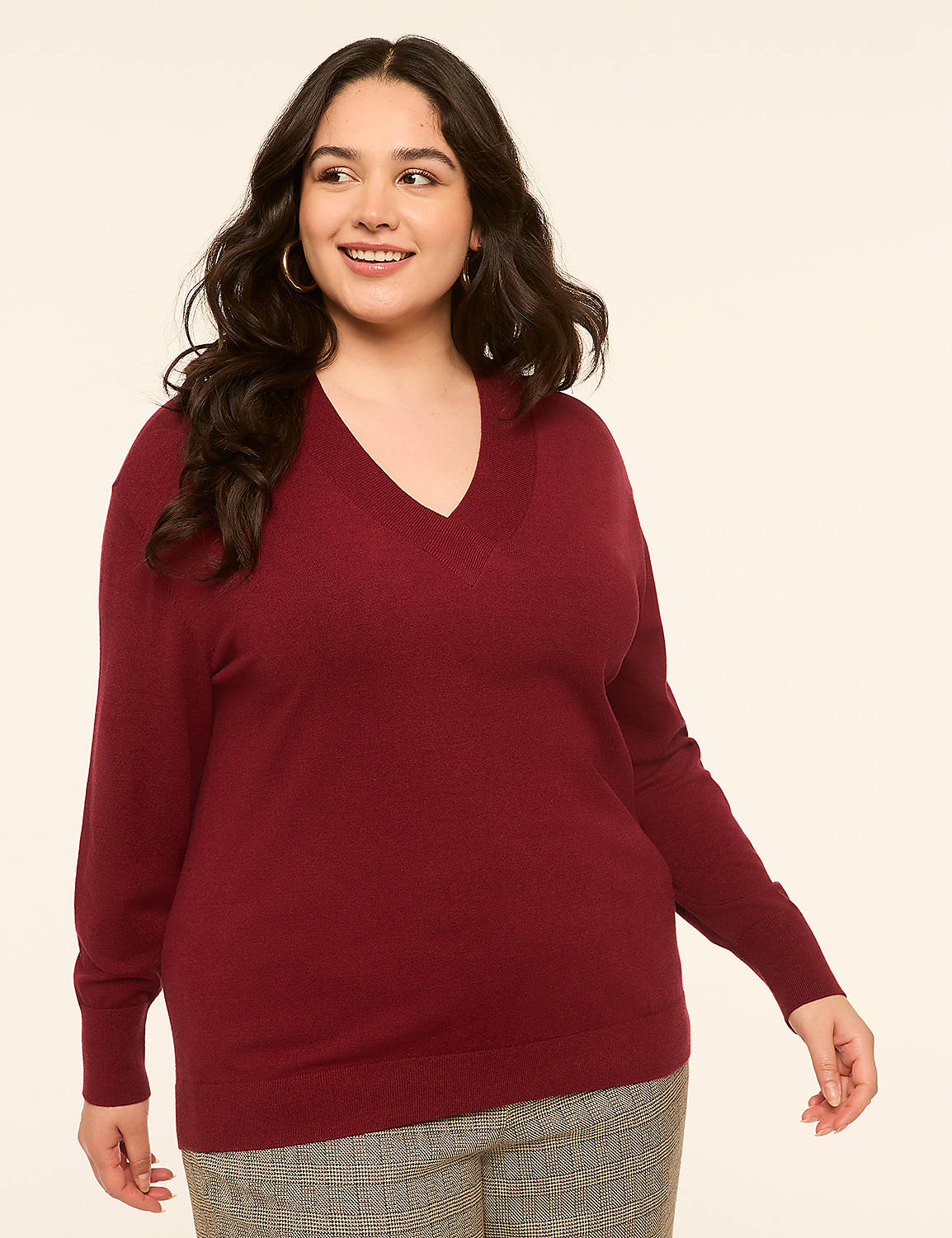 A smiling woman in a maroon v-neck sweater and plaid pants stands against a plain, light-colored background. Product Image 1